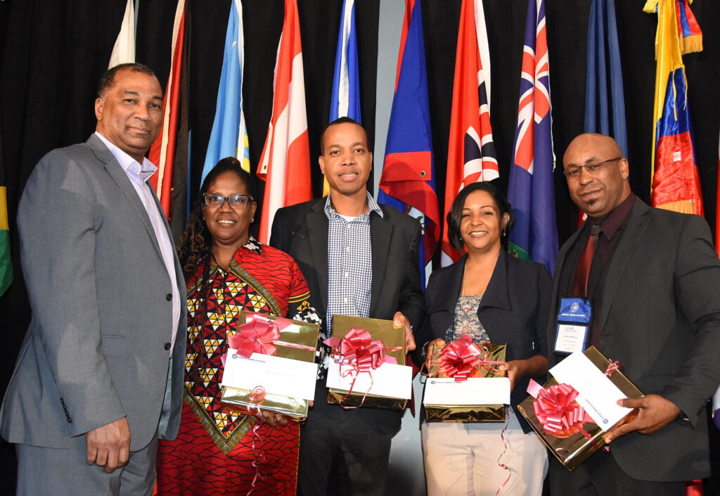 Five conference participants pose with wrapped gifts in front of national flags.