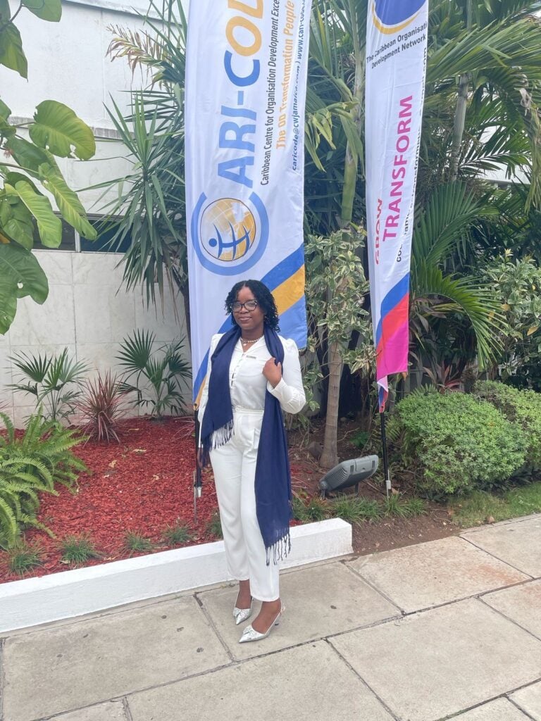 Conference attendee in a white suit standing beside Cari-Code banners.